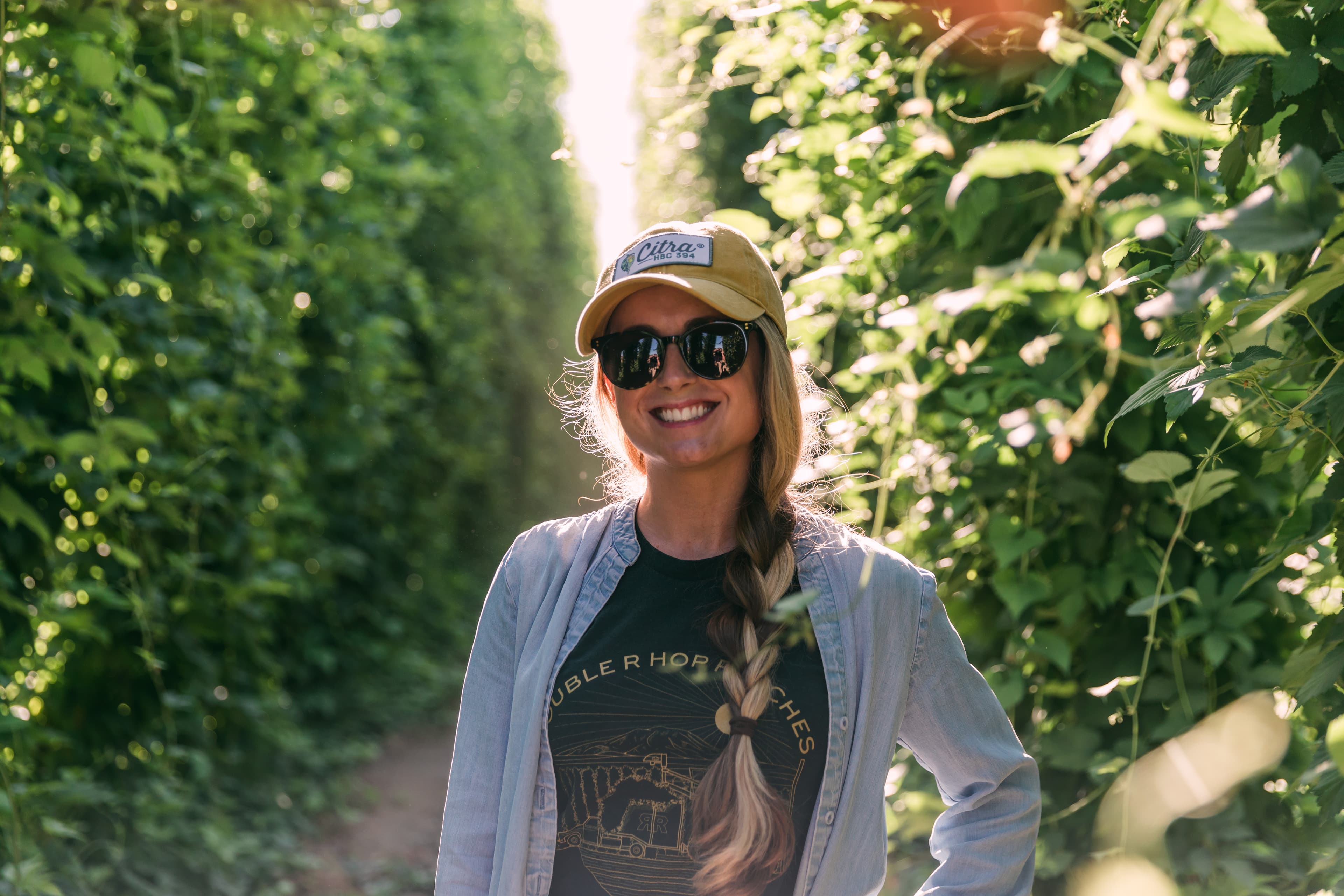 Woman smiles for a photo in front of a field of hops.