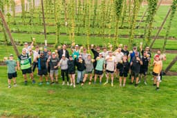 Group of runners in a hop field raising pints in a toast